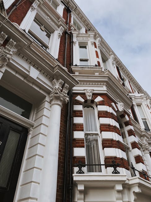 Exterior view of a row of white, multi-story residential buildings with ornate architectural details, including decorative cornices and pillars, situated on a street with parked cars and a leafless tree in the foreground. The scene is illuminated by daylight, with clear blue skies overhead. Shepherd's Bush Cleaners provides expert domestic and commercial cleaning, including end of tenancy cleaning services for properties like these, ensuring surfaces such as windows, facades, and balconies are thoroughly cleaned and maintained.